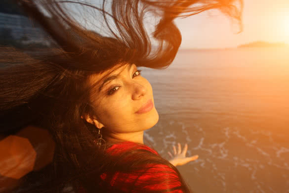 Young beautiful woman with flying hair at beach at sunset