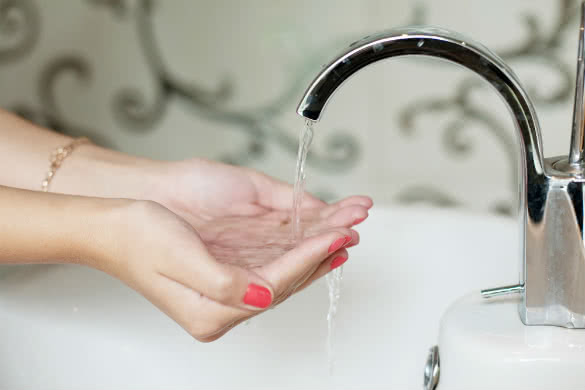 girl holding hands with red nails under tap of water
