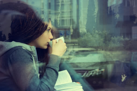 Young woman drinking coffee and reading book sitting indoor in urban cafe