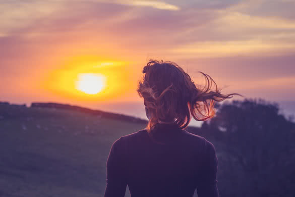Young woman admiring the sunset over fields