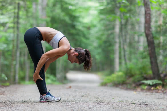 Athletic middle aged woman stretching in the green leaved woods on a dirt road before a run in Surry