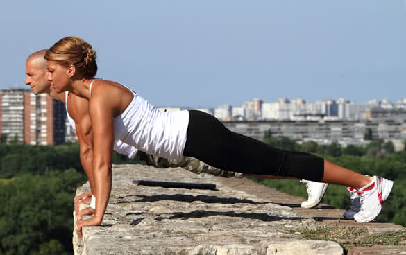Female and male fitness instructors doing pushups on the top of the stone wall