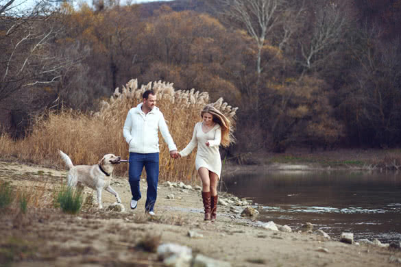 Young happy couple walking with dog near the lake in autumn