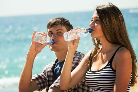 Thirsty young couple enjoying bottle of water at seashore in sunny day