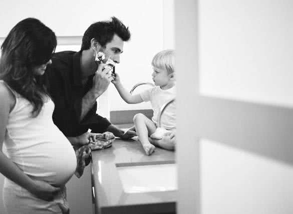 son helping father with shaving and happy pregnant mother