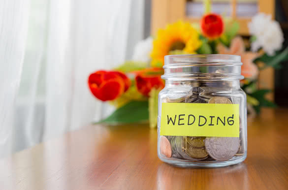 coins-in-a-money-jar-with-wedding-label-on-jar,-flowers-on-background