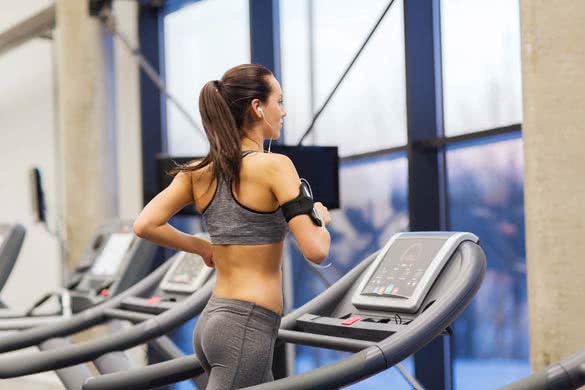 woman with smartphone or player and earphones exercising on treadmill in gym