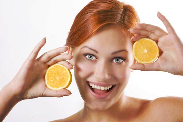 Beautiful girl holding two juicy lemons near her face