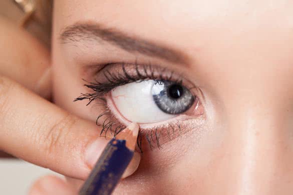 woman applying eyeliner on eyelid with pencil