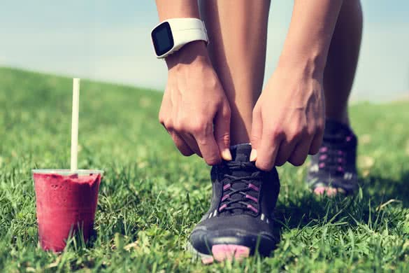 runner tying laces with fruit smoothie wearing smartwatch for cardio