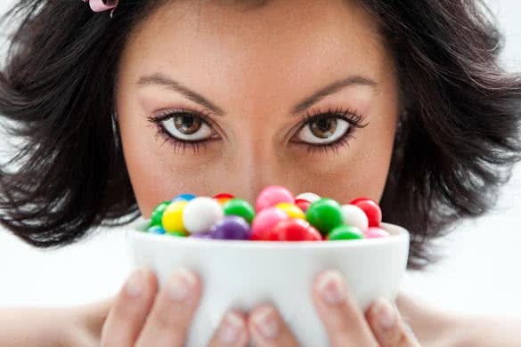 Beautiful candy girl closeup holding a bowl of colorful bubblegum candy balls in front of her face