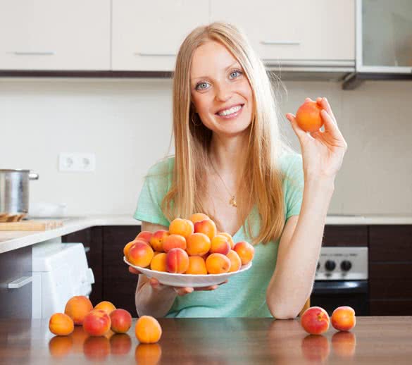 Happy young blonde housewife with heap of apricots