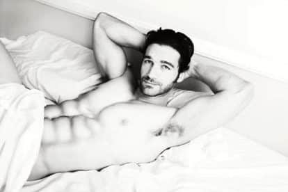 Young muscular male model lying back in bed with sexy smile