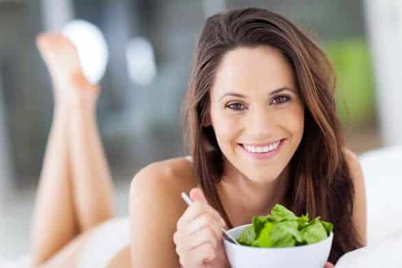 happy young woman eating green salad on bed