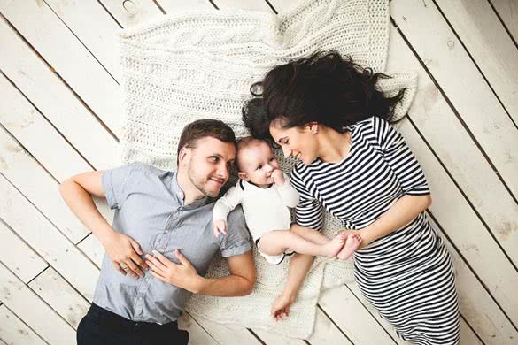 Happy young father mother and cute baby boy lying on rustic wooden floor