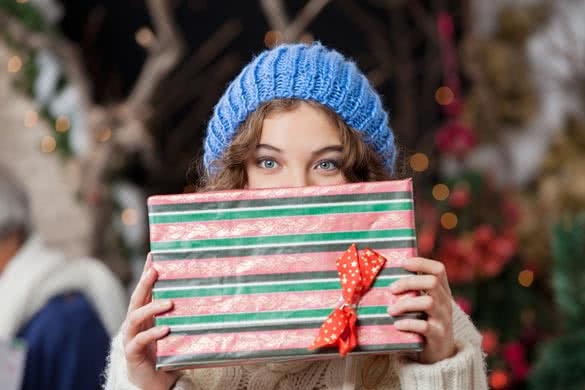 Portrait of beautiful young woman covering face with Christmas present at store