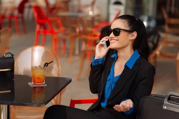 Cheerful business woman in sunglasses sitting at the cafe and talking on the phone