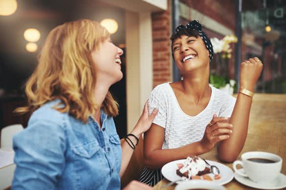 Two multiethnic young female friends enjoying coffee together in a restaurant laughing