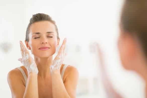 Young woman washing face in bathroom