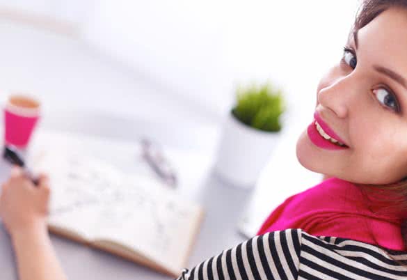 Young woman writes to diary on a white table