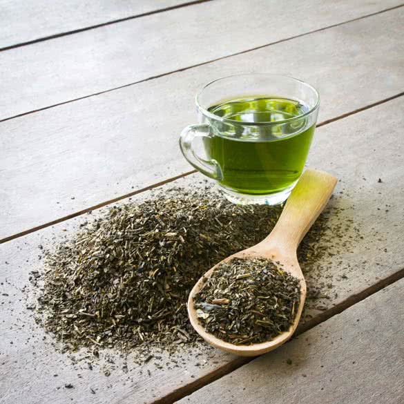 cup of green tea and spoon of dried green tea leaves on wooden background