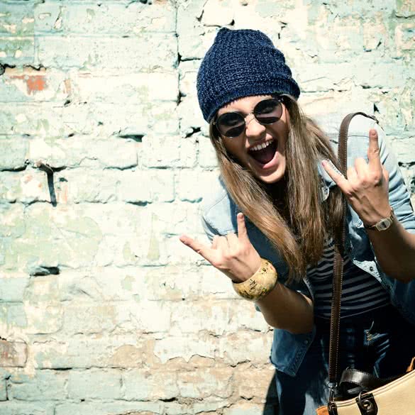 portrait of beautiful cool girl gesturing in hat and sunglasses over grunge wall