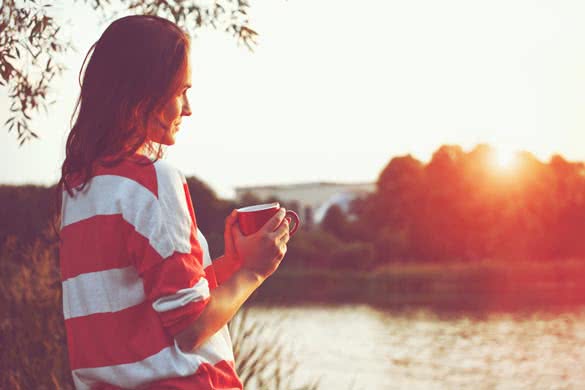 pretty girl with morning coffee at river sunrise
