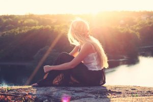 girl sitting on a cliff watching sunset