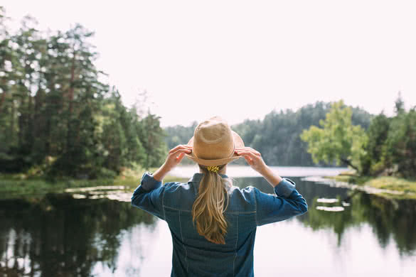 young woman in a straw hat standing by the lake in the woods