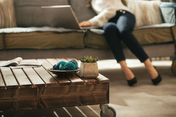 Closeup on coffee table and young woman using laptop in background