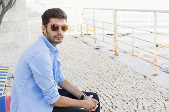 Handsome young man in bluejeans sitting on a bench nearby the sea