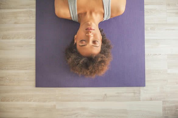 Indoor high-angle shot of an African woman lying on a yoga mat with her eyes closed