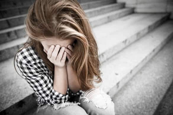 Unhappy depressed teenager with face in hands sitting outdoor