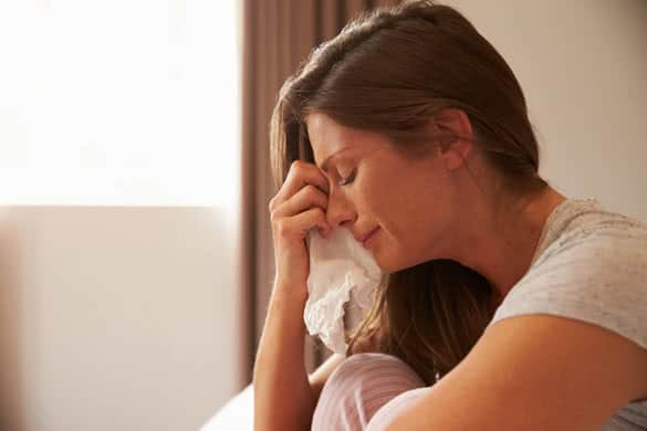 Woman Suffering From Depression Sitting On Bed And Crying