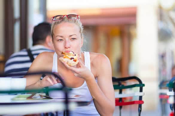 Casual blond lady eating pizza slice outdoor in typical italian street restaurant on hot summer day