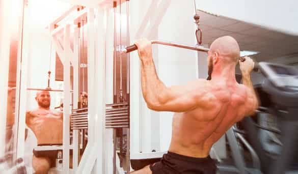 Man doing back pullups in the mirror at the gym with a energy powerful look and feel with soft filters applied suggesting a hard workout