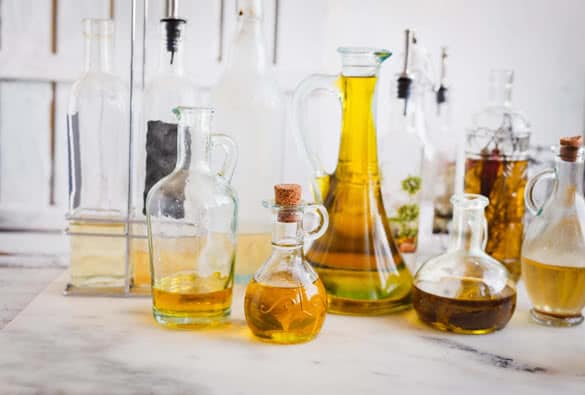 various bottles with raw olive oil with herbs and vinegar over on a marble rustic table