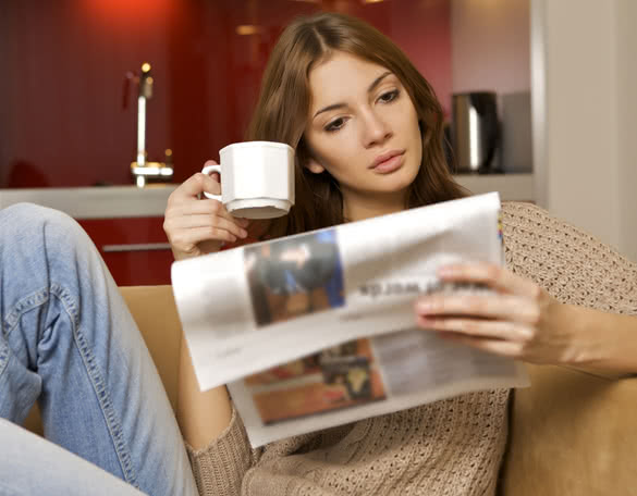young adult beautiful brunette woman drinking coffee and reading newspaper in luxury apartment