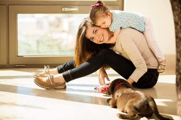 Beautiful young Hispanic mother with a baby girl and a cute Labrador puppy at home