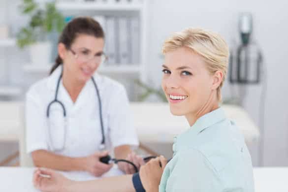 Doctor taking blood pressure of her smiling patient in medical office