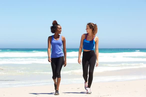 Full body portrait of two fit young women walking on beach