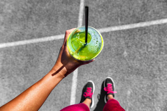 Green smoothie woman drinking plastic cup breakfast meal takeaway to go after morning run on city streets