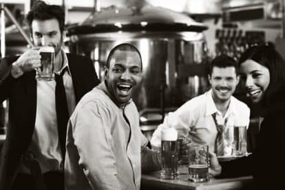 Happy friends having fun in pub watching sport in TV together drinking beer cheering for team
