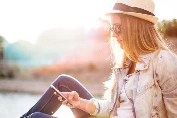 Hipster woman texting in sunset by the sea