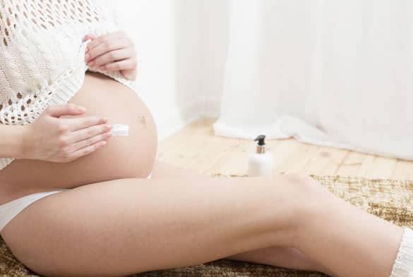 Pregnant woman putting cream on her belly to avoid stretch marks