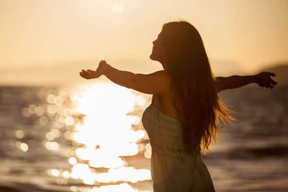 Pretty young woman enjoying a sunset at the beach with arms wide open