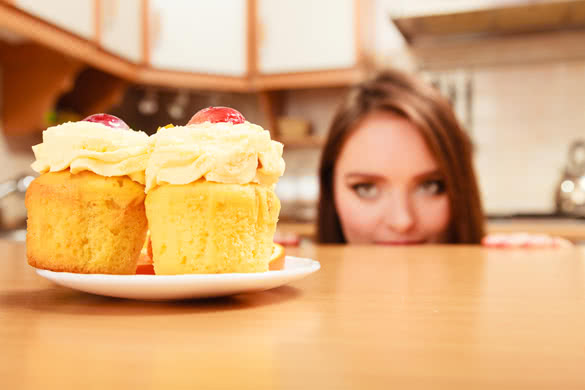 Woman hiding behind table sneaking and looking at delicious cake with sweet cream and fruits on top