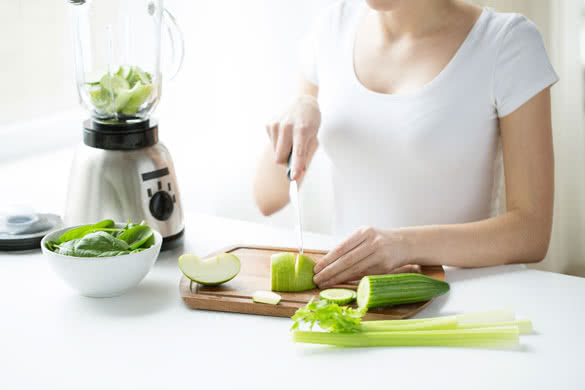 young woman with blender chopping green vegetables for detox shake or smoothie at home