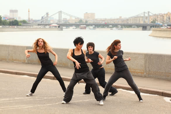 Four girls in same black clothes dancing on embankment on background of bridge