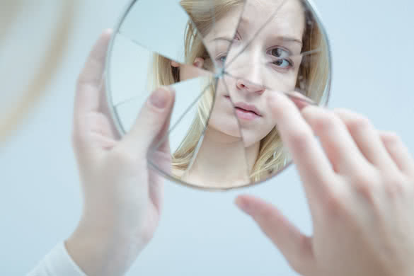 Insecure pretty young woman holding broken mirror